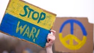 Ein Hand hält ein gelb-blaues Schild in die Luft auf dem "Stop War!" steht. © picture alliance / Geisler-Fotopress I Sebastian Gabsch/Geisler-Fotopress Foto: Sebastian Gabsch/Geisler-Fotopress