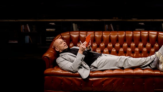 Ein Mann liegt auf einem braunen Ledersofa und blickt auf ein Tablet. © NDR Foto: Janine Meyer