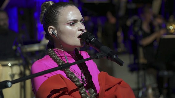 Screenshot: Sängerin Inéz vom Pop-Duo ÄTNA singt auf der Bühne der Elbphilharmonie während eines Konzerts mit der NDR Bigband. © NDR Bigband Foto: Screenshot