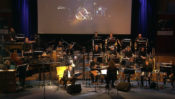 Screenshot: Erzähler Stefan Schade, Wolf Kerschek und die NDR Bigband beim "Hamburger Zeitmärchen" © NDR 