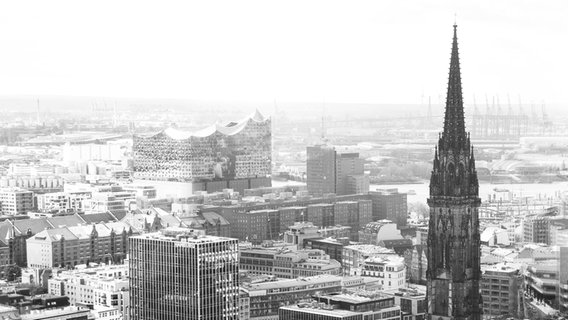 Eine schwarz-weiß-Fotografie: Hamburg vom oben; im Vordergrund der Kirchturm von St. Nikolai, im Hintergrund die Elbphilharmonie. © Internationales Musikfest Hamburg 