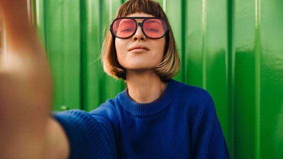Eine Frau mit einer Brille mit rosaroten Gläsern im Porträt. © NDR/Adobe Stock Foto: NDR/Adobe Stock