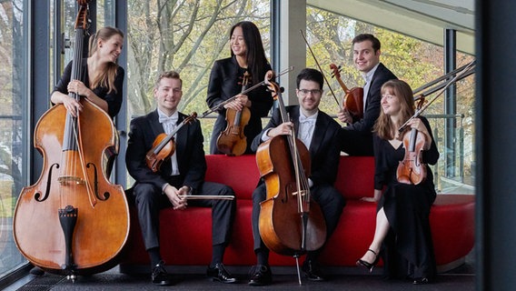 Junge Musikerinnen und Musiker mit Streichinstrumenten auf einem roten Sofa © NDR Foto: Micha Neugebauer