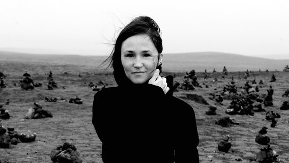 Komponistin Anna Thórvaldsdóttir steht inmitten einer kargen Landschaft (schwarz/weiß). © Saga Sigurðardóttir 