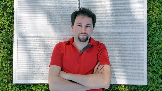 Im Porträt: Komponist Vito Žuraj liegt auf einer grpßen Partitur auf einer Wiese  Foto: Hans Christian Schinck
