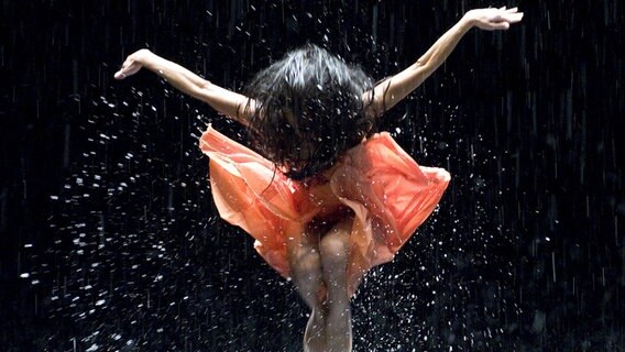 Szene aus dem Film "Pina": Eine Frau im orangefarbigen Kleid springt hoch und breitet die Arme aus. © picture alliance / dpa | Donata Wenders 