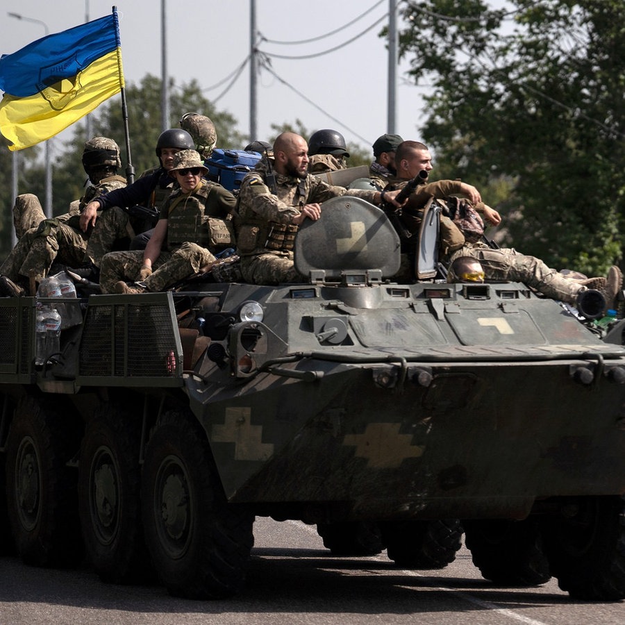 Ukrainische Soldaten fahren auf einem gepanzerten Fahrzeug auf einer Straße. © picture alliance/dpa/AP | Leo Correa 