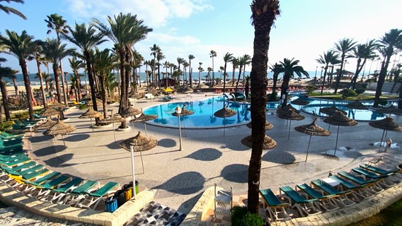 Blick auf einen leeren Hotelpool mit vielen leeren Sonnenliegen und Palmen. © NDR 