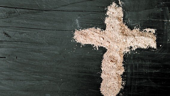 Ein Kreuz aus Asche auf dunklem Hintergrund © fotolia.com Foto: czarny_bez