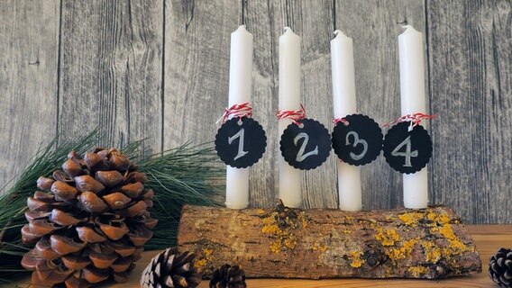 Ein Holzscheit mit vier weißen Kerzen, die Anhänger mit den Ziffern 1 bis 4 zeigen. © NDR Foto: Anja Deuble