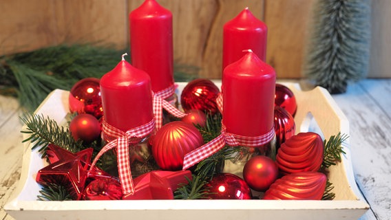 Vier rote Kerzen mit rotem Baumschmuck auf einem weißen Tablett. © NDR Foto: Anja Deuble