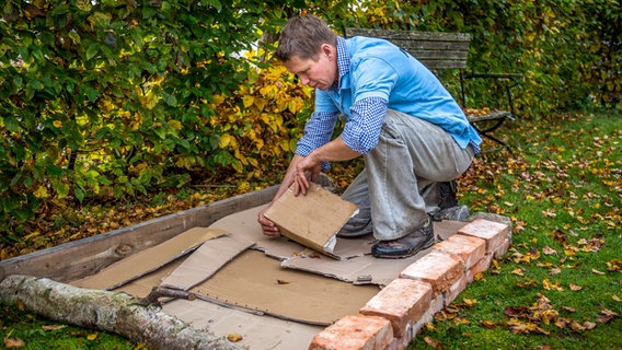 Peter Rasch legt Pappe in einen Rahmen aus Steinen und Holz. © NDR Foto: Udo Tanske