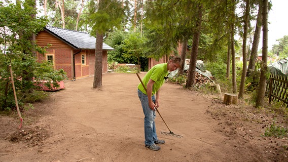 Gärtner Rasch arbeitet den Grassamen mit der Harke in den Boden ein. © NDR Foto: Udo Tanske