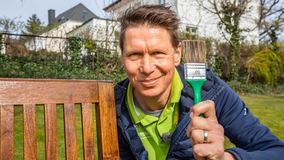 Peter Rasch hält einen Pinsel hoch. © NDR Foto: Jan-Philipp Baumgart