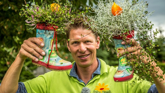 Gärtner Peter Rasch hält zwei bepflanzte Kindergummistiefel in die Luft. © NDR Foto: Udo Tanske