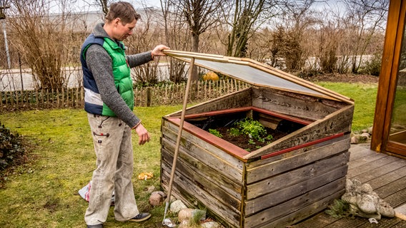 Peter Rasch stützt den Deckel des Hochbeets mit einem Gartengerät ab. © ndr.de Foto: Udo Tanske