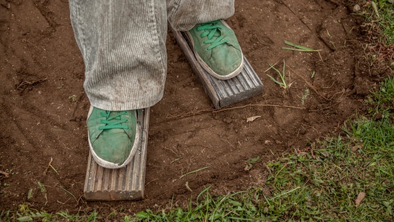 Schuhe mit angenagelten Brettern zum Verdichten von Boden. © NDR Foto: Udo Tanske