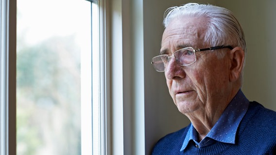 Ein alter Mann schaut aus einem Fenster hinaus. © colourbox 