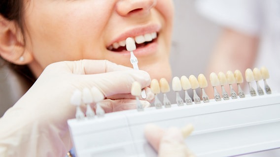 Einer Frau werden beim Zahnarzt verschiedene Zahnfarben gezeigt. © picture alliance/Zoonar Foto: Robert Kneschke