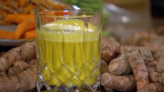 Ein Glas mit Goldener Milch steht vor Kurkuma-Wurzeln. © NDR Foto: Screenshot NDR