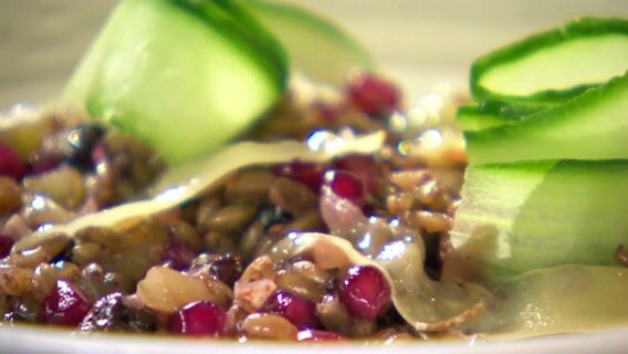 Granatapfel-Grünkern-Risotto angerichtet mit Gurkenscheiben.  