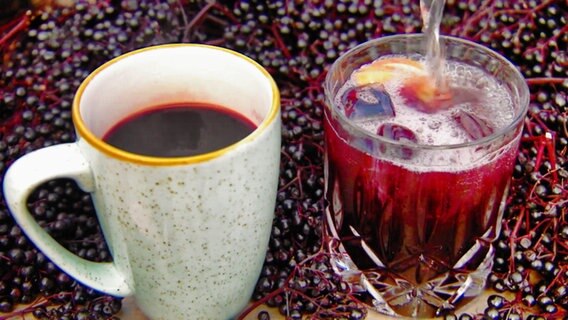 Heißer Holunderpunsch im Becher und Holundersaft mit Eiswürfeln im Glas.  