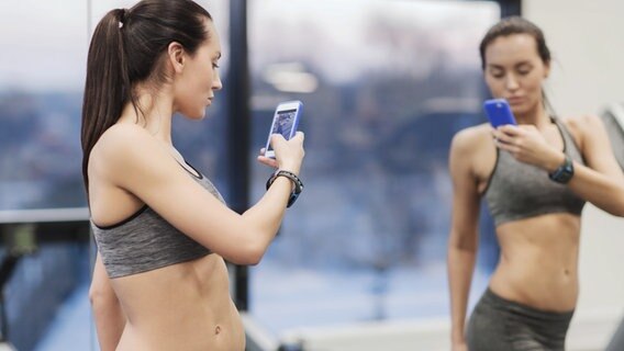 Eine durchtrainierte Frau im Fitnessstudio fotografiert ihr Spiegelbild. © Panthermedia Foto: Panthermedia | dolgachov