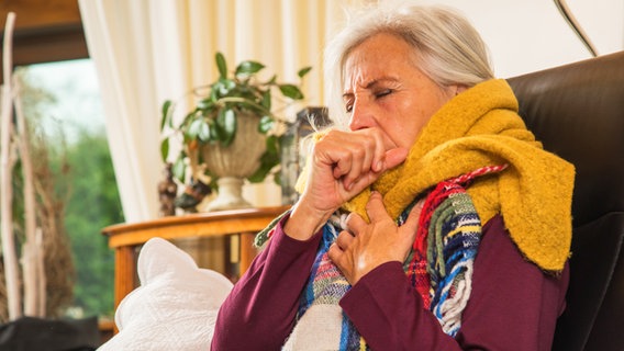 Eine ältere Frau sitzt mit Erkältungssymptomen auf einem Sofa. © picture alliance/dpa-tmn Foto: Christin Klose