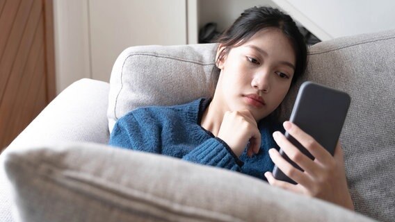 Ein auf dem Sofa sitzendes, junges Mädchen schaut sorgenvoll auf ihr Smarthphone Ein auf dem Sofa sitzendes, junges Mädchen schaut sorgenvoll auf ihr Smarthphone © wichayada (YAYMicro) / Panthermedia Foto: wichayada (YAYMicro) / Panthermedia