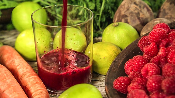 Ein selbstgemachter Rote-Bete-Shot im Glas steht neben Himbeeren, Limetten und Karotten. © NDR 