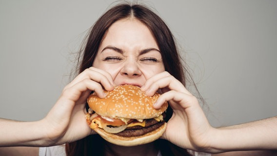 Eine Frau beißt in einen Burger. © Picture Alliance Foto: picture alliance / Bildagentur-online/Blend Images | Blend Images/Dmitry Ageev