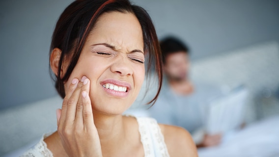 Eine Frau fasst sich mit schmerzverzerrtem Gesicht an den Kiefer. © IMAGO / YAY Images Foto: IMAGO / YAY Images
