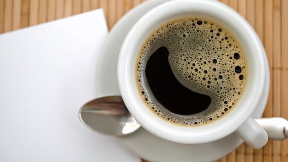 Eine Tasse Kaffee steht auf einem Bambusset, daneben liegt Schreibpapier. © Colourbox Foto: Y. Haivoronska