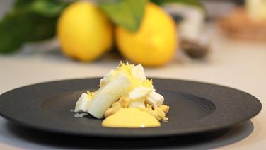 Zitronenmousse, Nussbutter-Espuma, Baiser und Vanillestreusel auf einem schwarzen Teller angerichtet. © Thomas Mudersbach / solisTV 