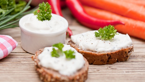 Zwei kleine Brotscheiden sind mit Frischkäse bestrichen und mit Petersilie dekoriert. © COLOURBOX Foto: JuNiArt