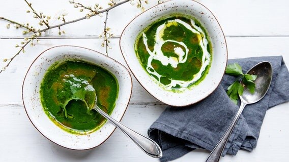 Zwei Keramikschalen mit grüner Spinatsuppe auf einem weißen Holzbrett. © NDR Foto: Claudia Timmann