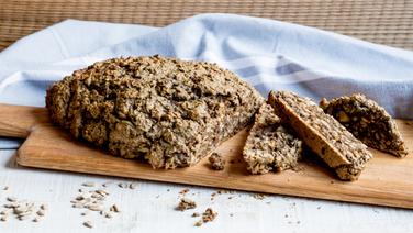 Auf einem Tischtuch  liegt ein Holzbrett mit angeschnittenem Körnerbrot. © NDR Foto: Claudia Timmann