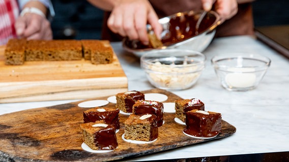 Kleine Würfel von braunem Kuchen werden auf Oblaten gesetzt und verziert. © NDR Foto: Claudia Timmann