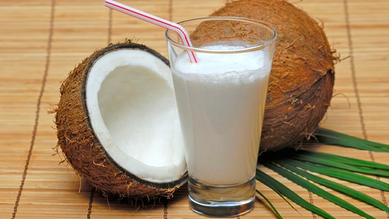 Ein Glas mit Kokosmilch, dahinter eine aufgeschnittene Kokosnuss. © picture alliance / imageBROKER Foto: J. Pfeiffer