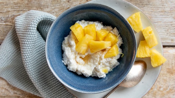 Ein Schälchen mit Reis-Porridge, darauf eine Stücke Ananas. © NDR Foto: Claudia Timmann