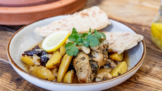 Tajine mit Huhn und ein Stück Brot auf einem Teller serviert. © NDR Foto: Claudia Timmann