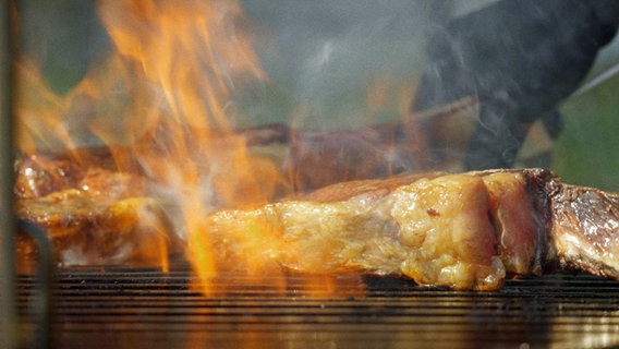 Ein Tomahawk-Steak wird über offenem Feuer gegrillt. © NDR 