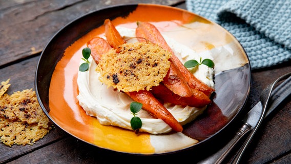 Geschmorte Möhren mit Orangenquark und Parmesanplätzchen auf einem Teller serviert © NDR Foto: Claudia Timmann