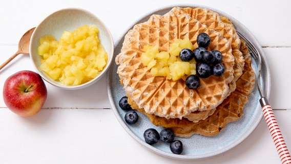 Buchweizen-Waffeln auf einem Teller, daneben und darauf Apfelmus und einige Blaubeeren. © NDR Foto: Claudia Timmann