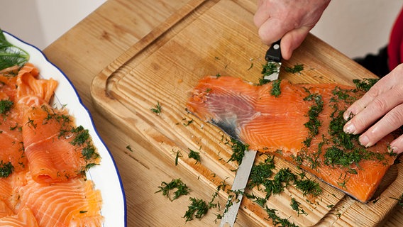 Gebeitzter Lachs wird mit einem langem Messer auf einem Brett geschnitten. © NDR Foto: Claudia Timmann