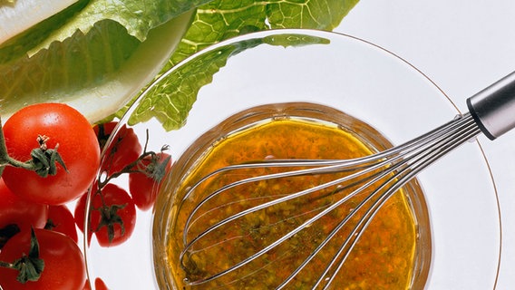 Eine Vinaigrette wird mit einem Schneebesen in einer Glasschüssel angerührt. © Stockfood Foto: Susie Eising