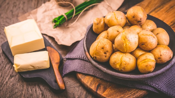 Gekochte Kartoffeln, daneben ein Stück Butter, im Hintergrund frischer Schnittlauch. Gekochte Kartoffeln, daneben ein Stück Butter, im Hintergrund frischer Schnittlauch. © Colourbox