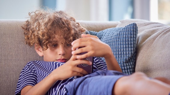 Ein Junge liegt mit seinem Smartphone auf dem Sofa © Colourbox Foto: #821