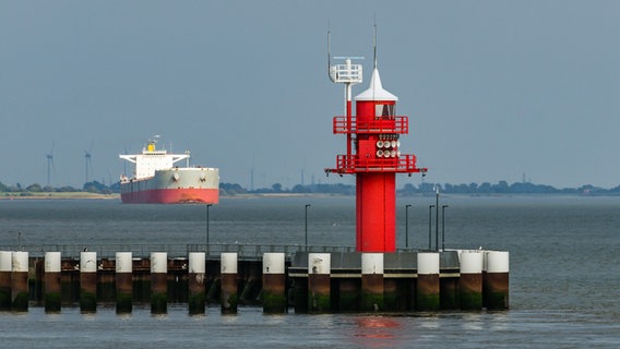 Ein Frachtschiff fährt auf der Elbe an einem roten Leuchtturm vorbei. © Picture Alliance / Zoonar Foto: Conny Pokorny