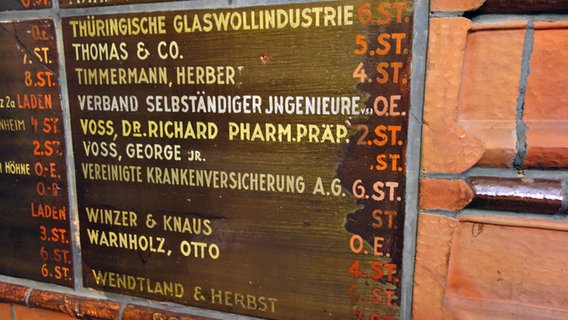 Auf einem alten Schild im Treppenhaus des Chilihauses stehen handgeschriebene Namen von Firmen und Mietern. © NDR Foto: Kathrin Weber